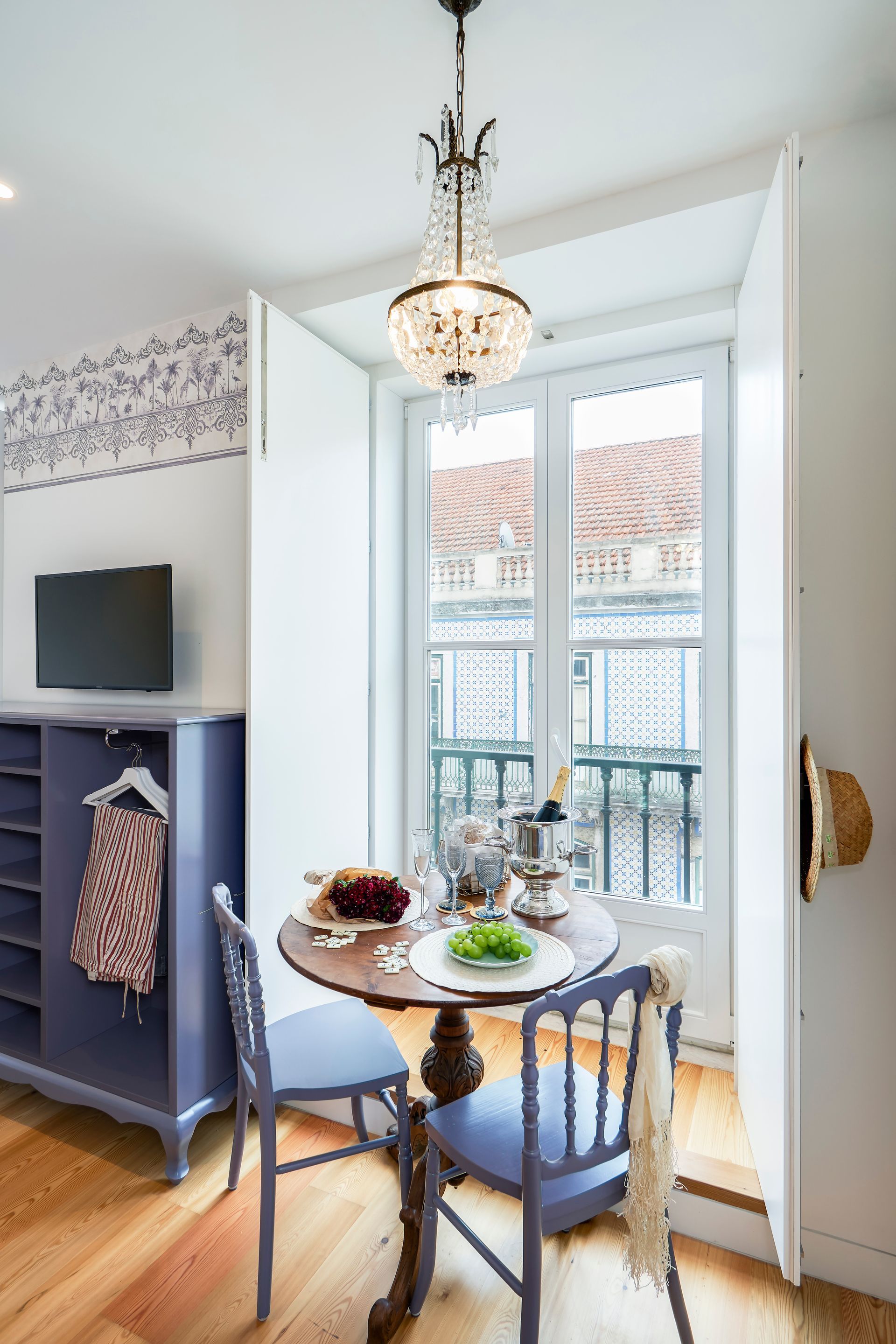 Small dining area with a round table, two blue chairs, and a window overlooking a street.