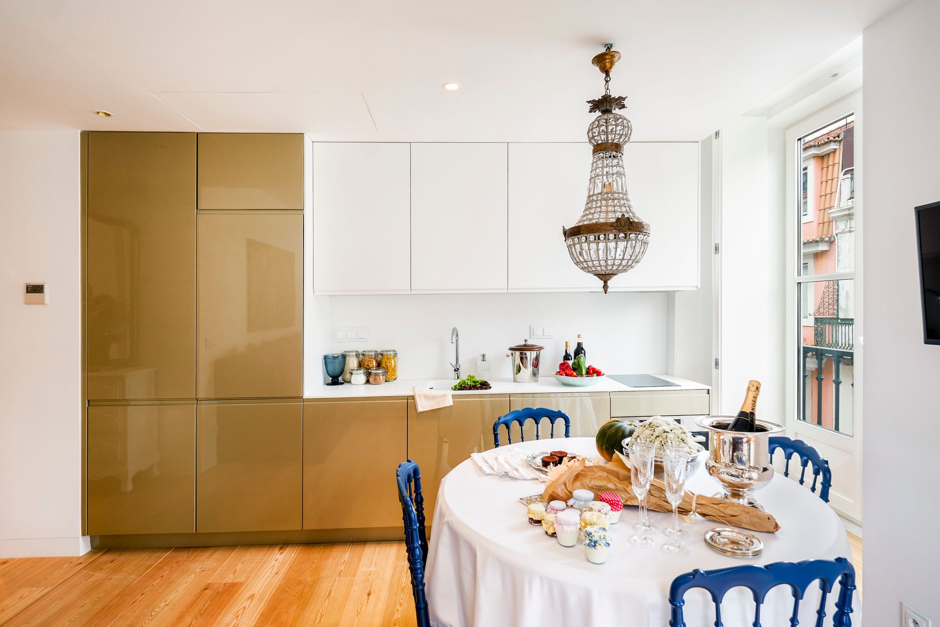 Kitchen with white and gold cabinets, dining table with blue chairs, and a chandelier.
