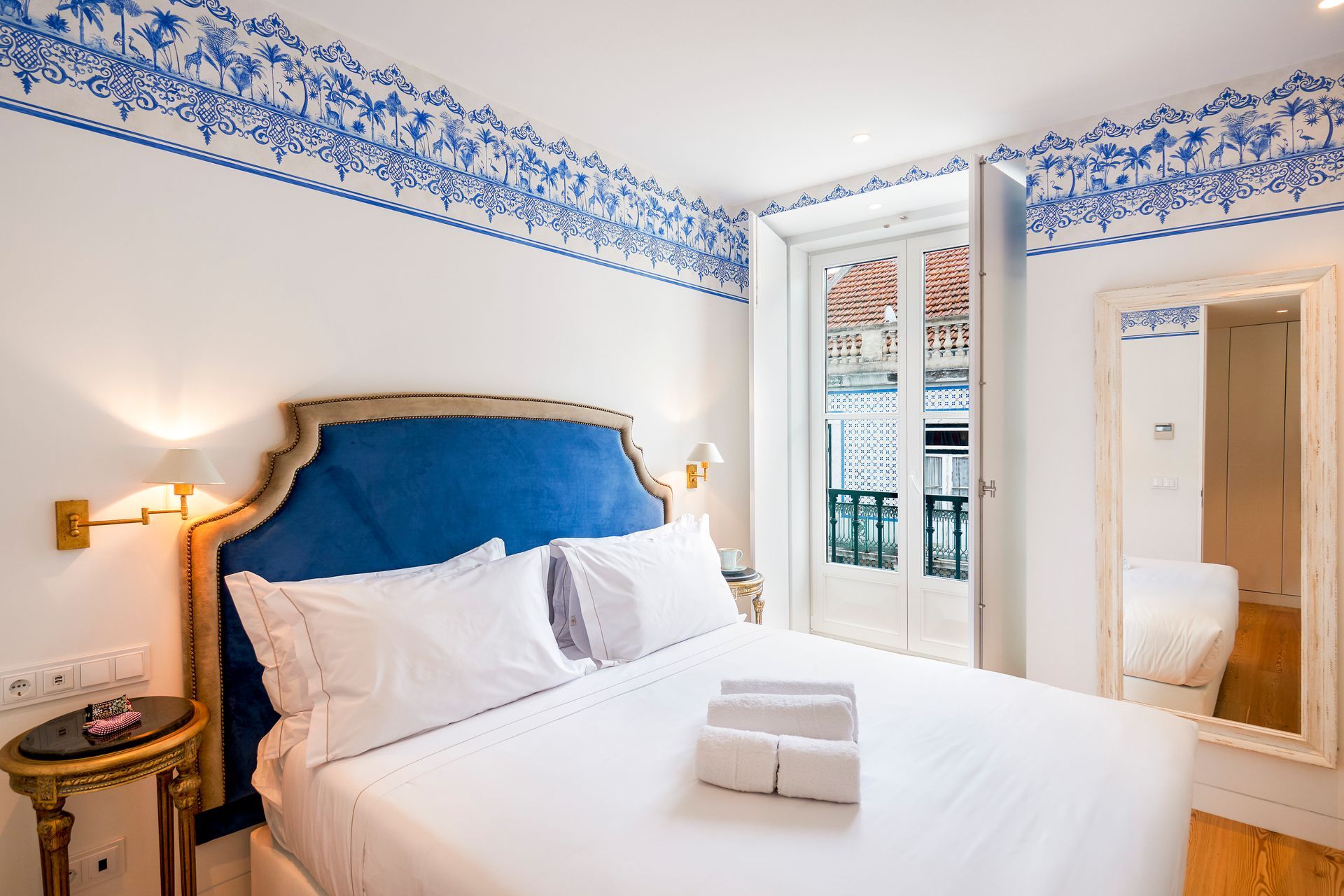 Bedroom with blue and white decor; bed with white linens, balcony door open, and a mirror.