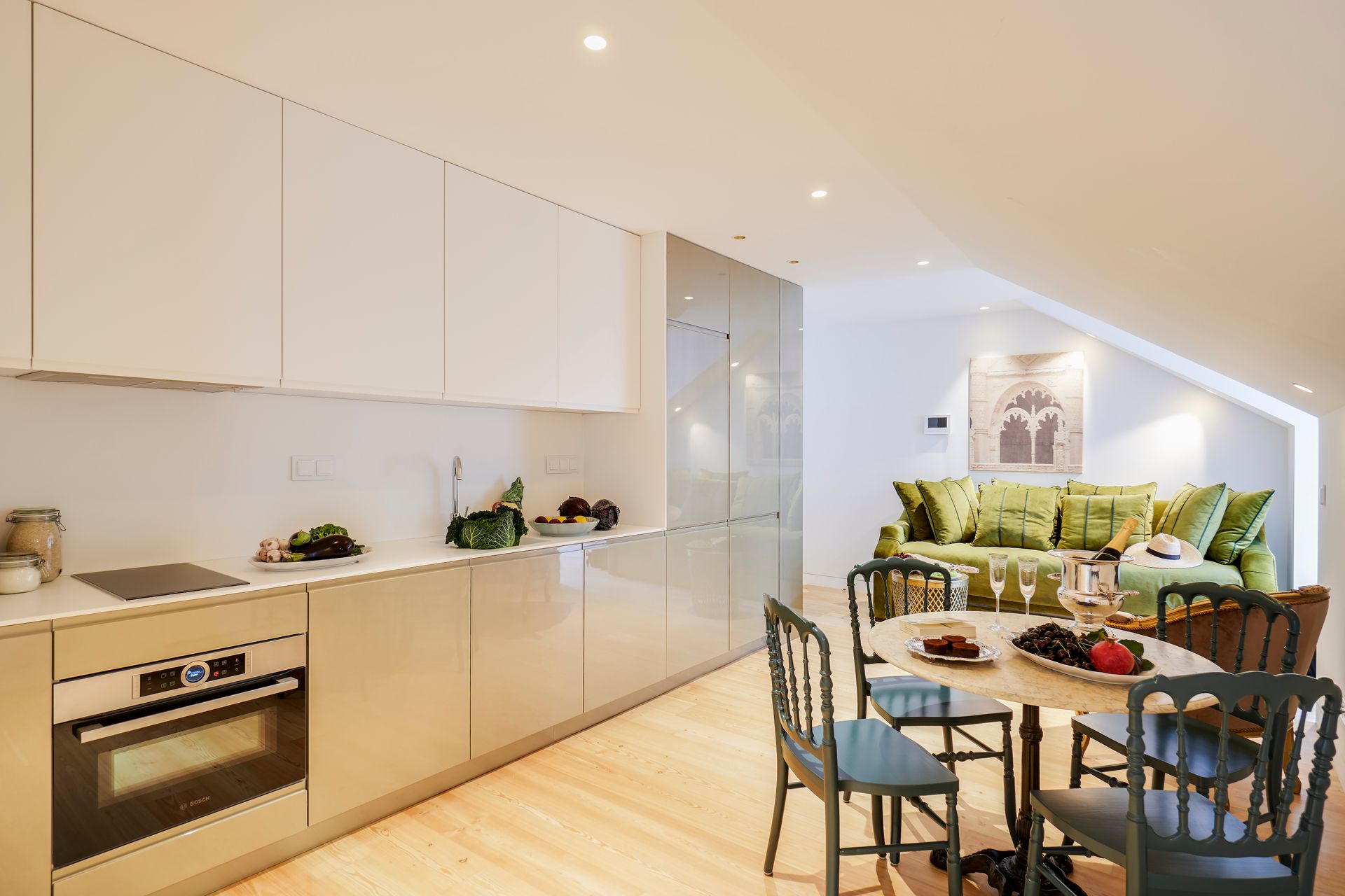 Kitchen and dining area with light cabinets, a round table, and a green velvet sofa.