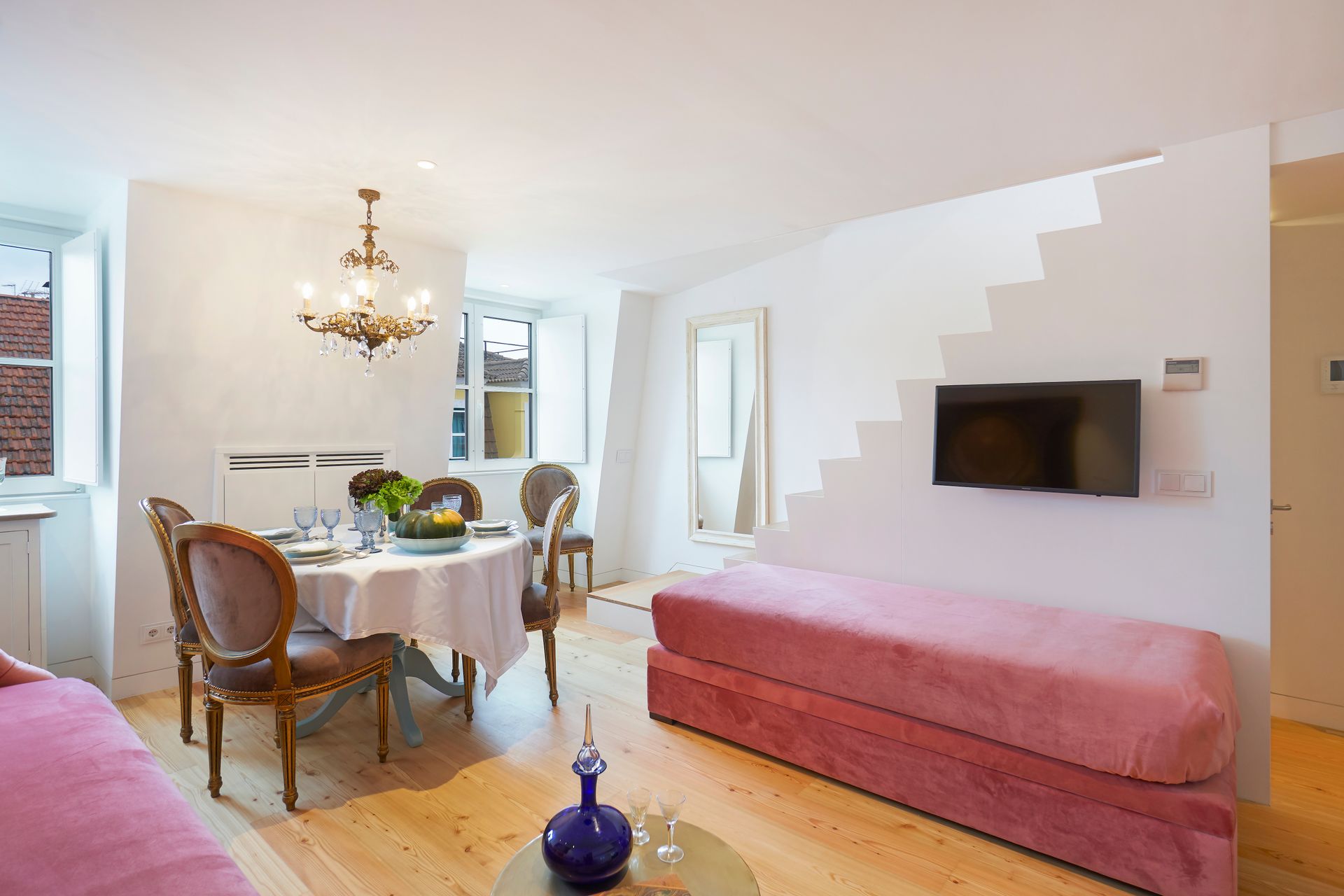 Living room with a dining table, pink sofa, TV, and staircase-like design on the wall.