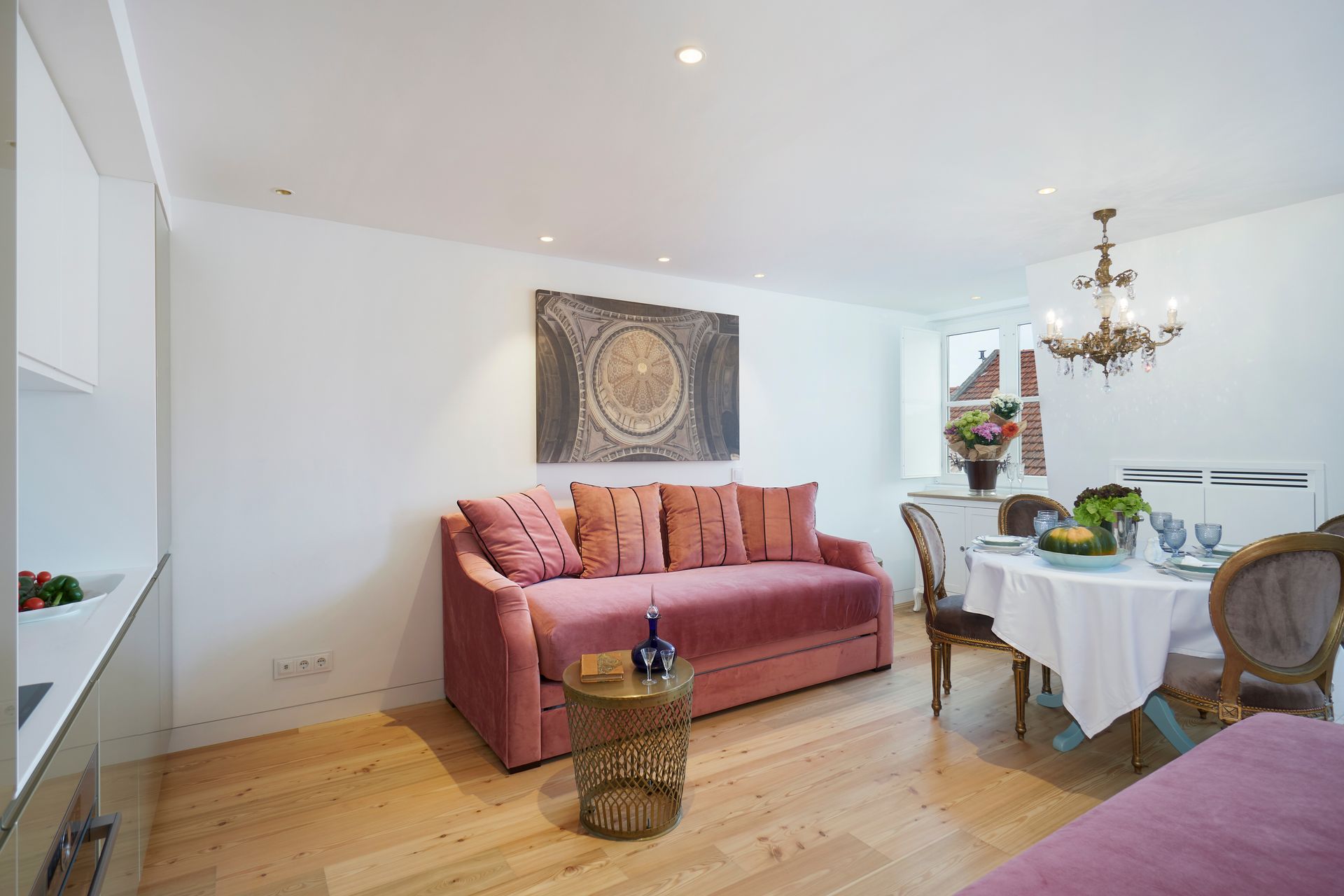 Living room with pink sofa, dining table, and artwork on a white wall.