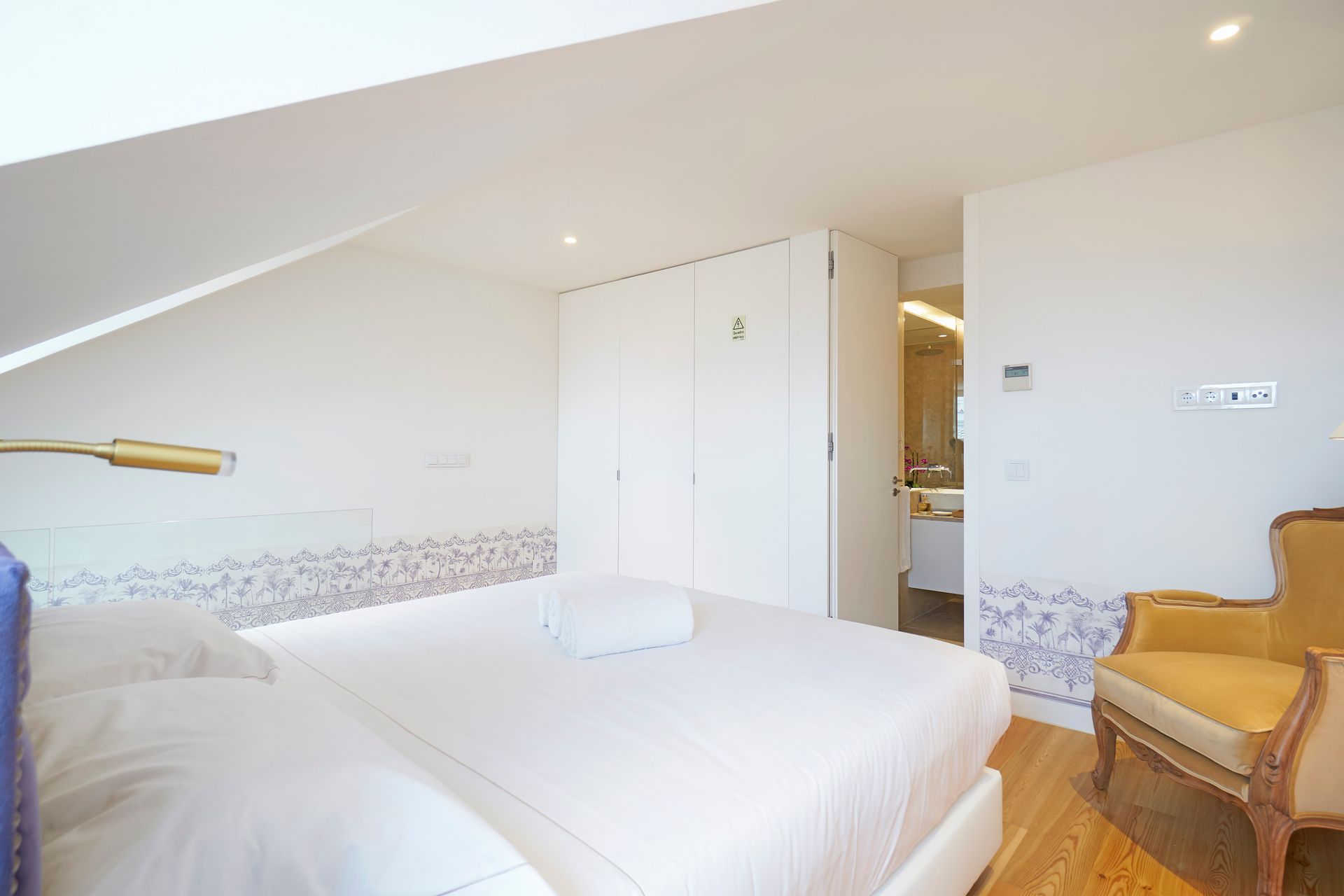 Bedroom with bed, closet, and a bathroom visible through a doorway. Yellow chair sits to the right.