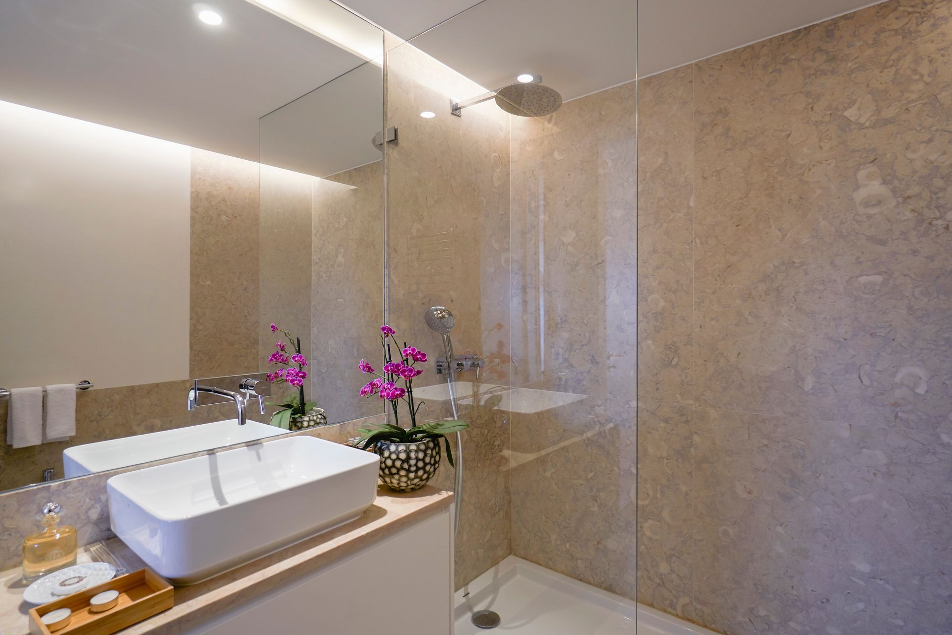 Modern bathroom with a white sink, glass shower, and beige stone walls.