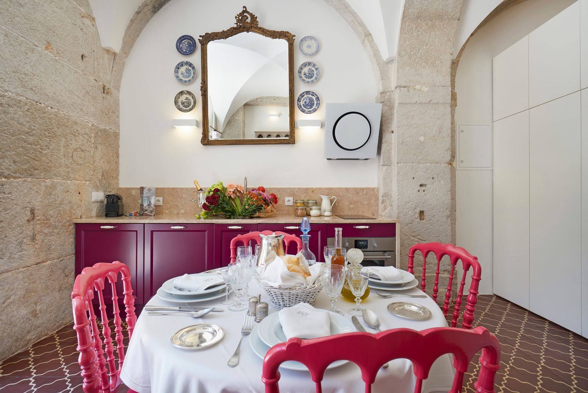 Dining room with set table and red chairs. Pink cabinets, decorative plates, and arched ceiling.