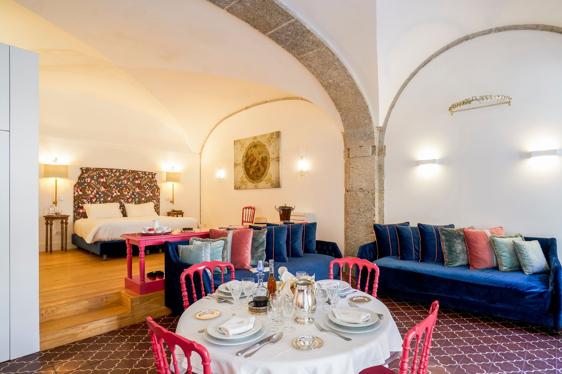 Hotel suite interior with a dining area, living space with blue sofas, and a bedroom.
