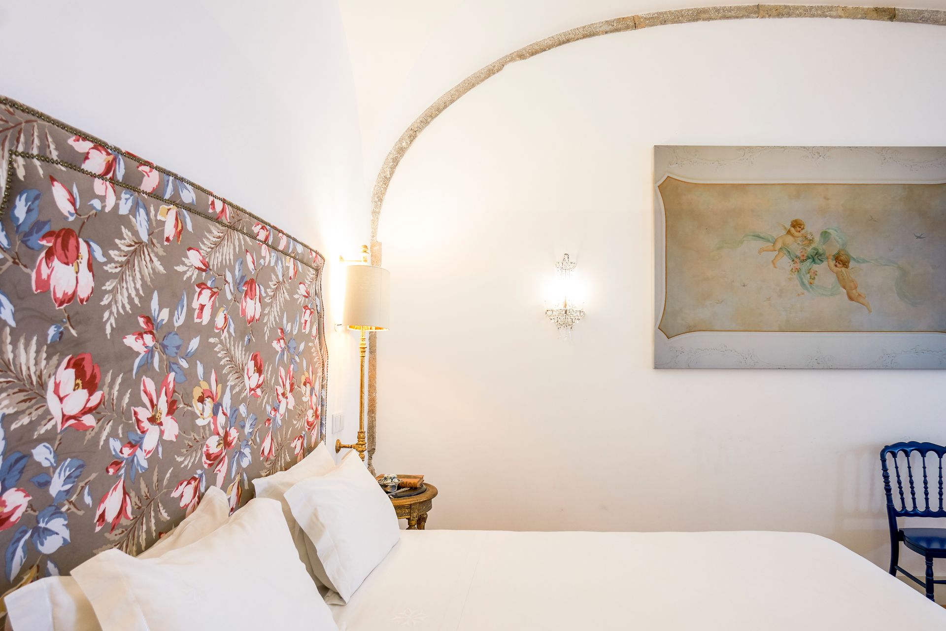 Bedroom with floral headboard, arched ceiling, and artwork. Blue chair on the right.