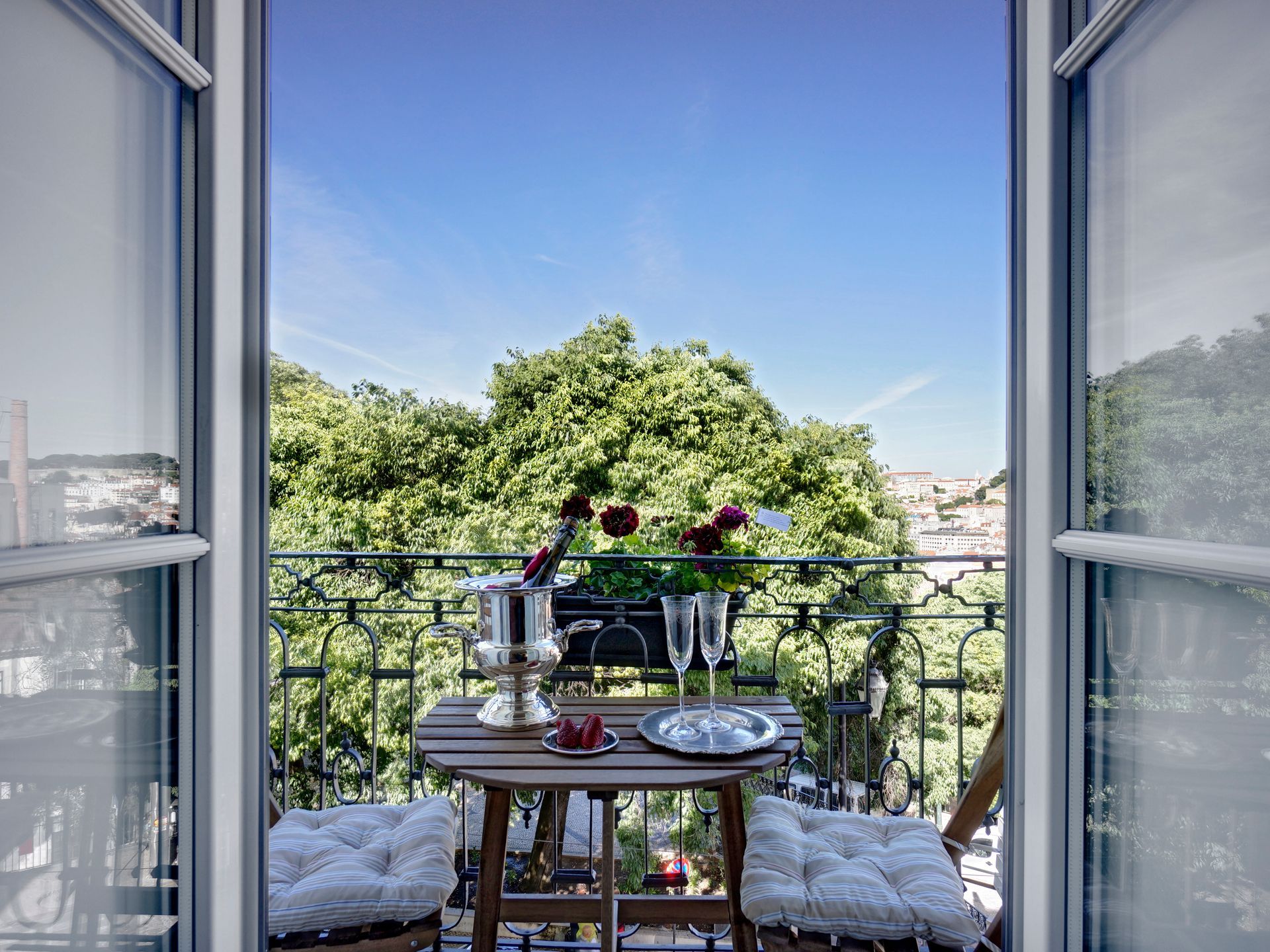 Balcony view from a premium one-bedroom apartment with a table set for two and lush green surroundings.