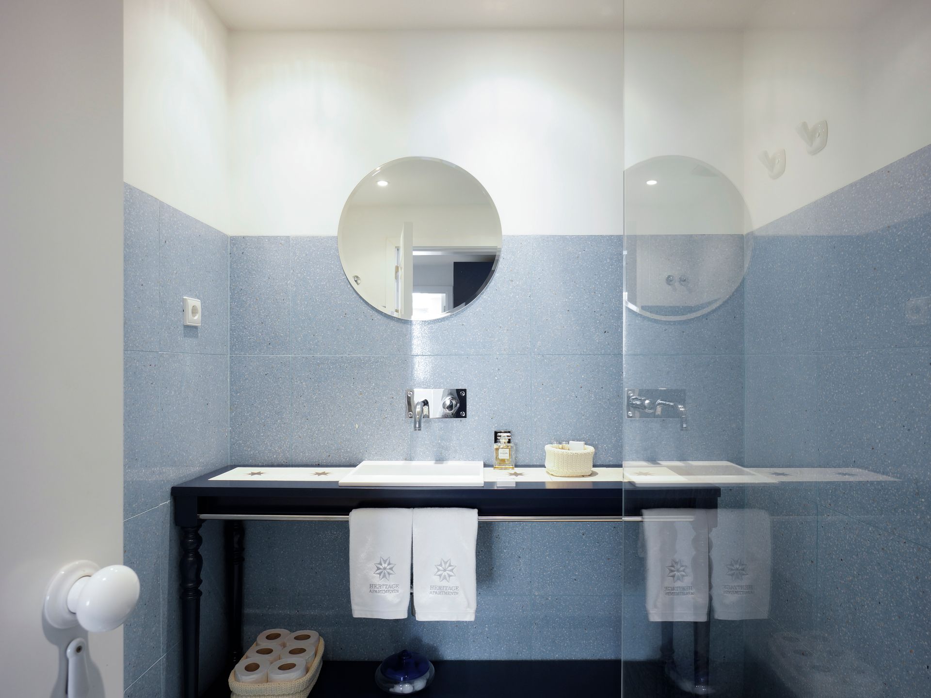 Modern bathroom in a premium one-bedroom apartment with blue tiles, a round mirror, and elegant amenities.