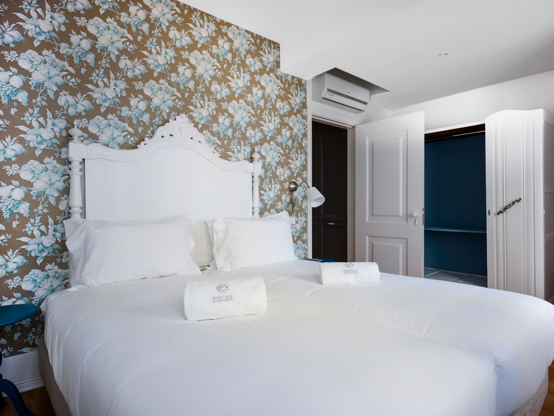 Stylish bedroom with floral wallpaper and white bedding in a spa deluxe two-bedroom apartment.