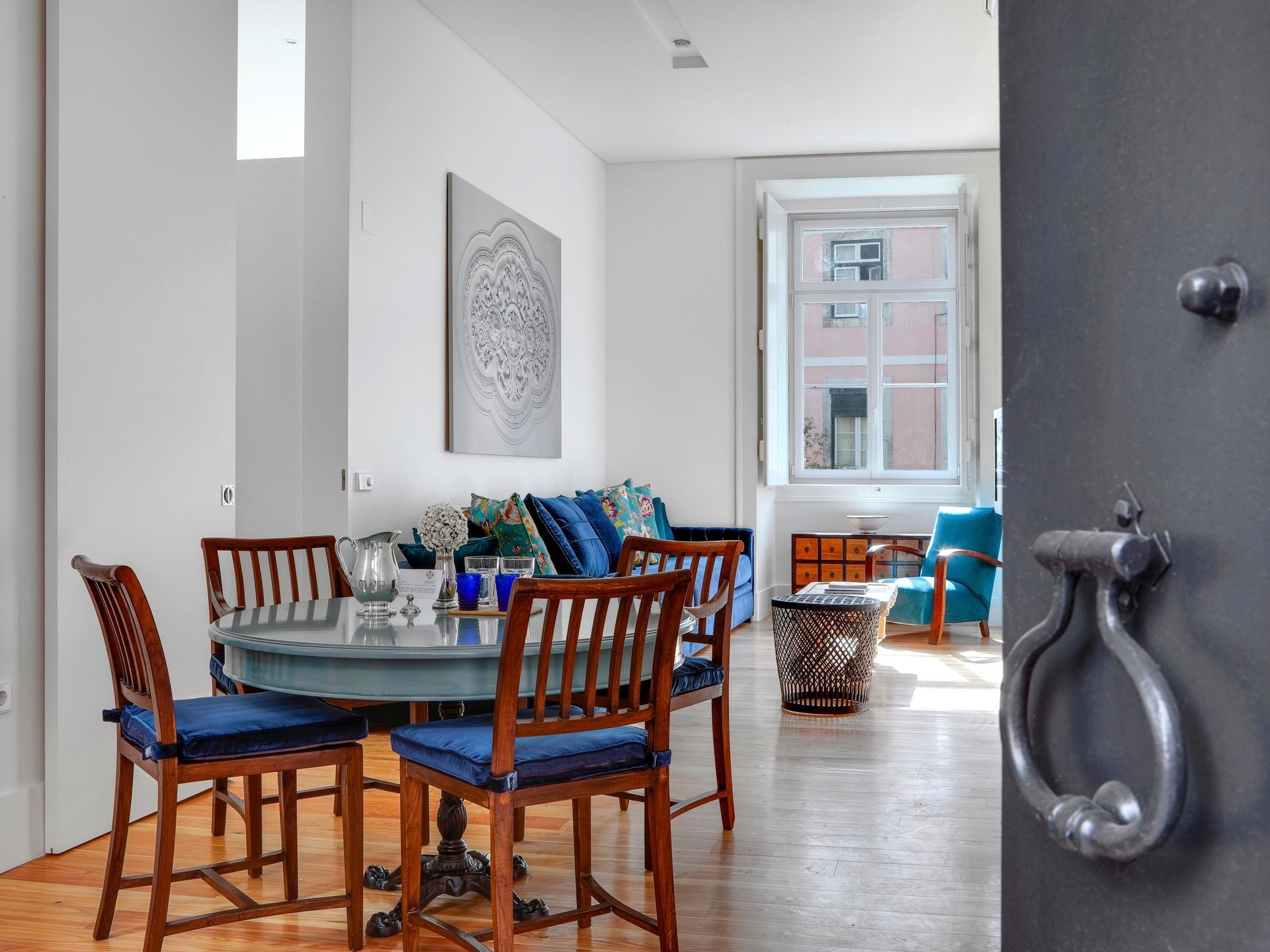 Dining area in a deluxe one-bedroom apartment with wooden chairs, a blue table, and decorative glassware.