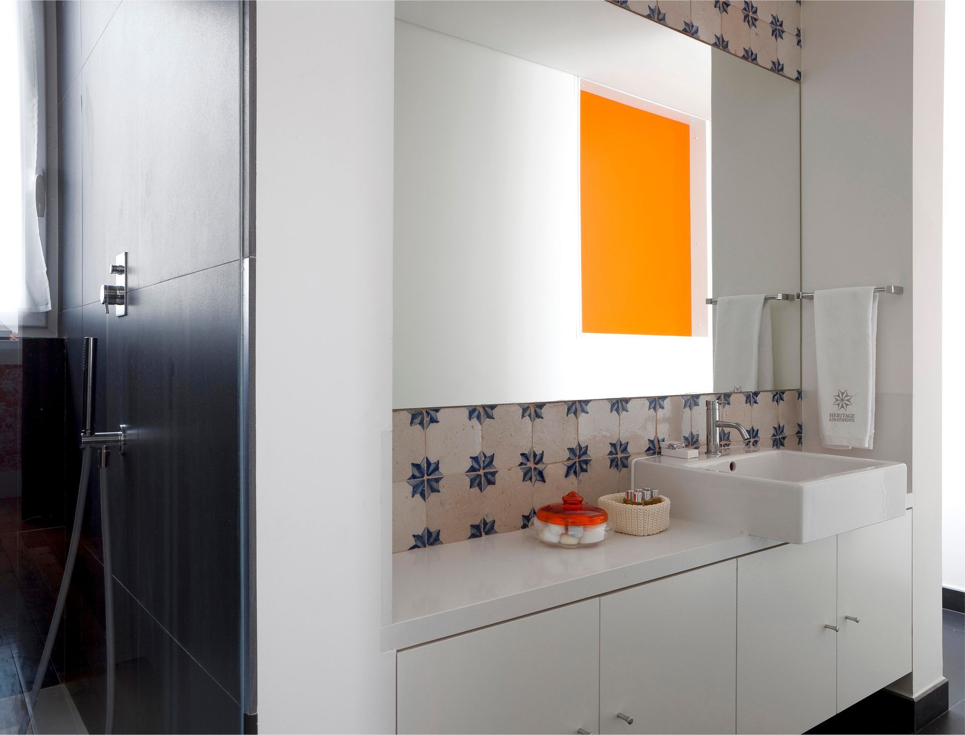 Stylish bathroom with orange accent wall, mirror, and decorative tiles in a duplex one-bedroom apartment.