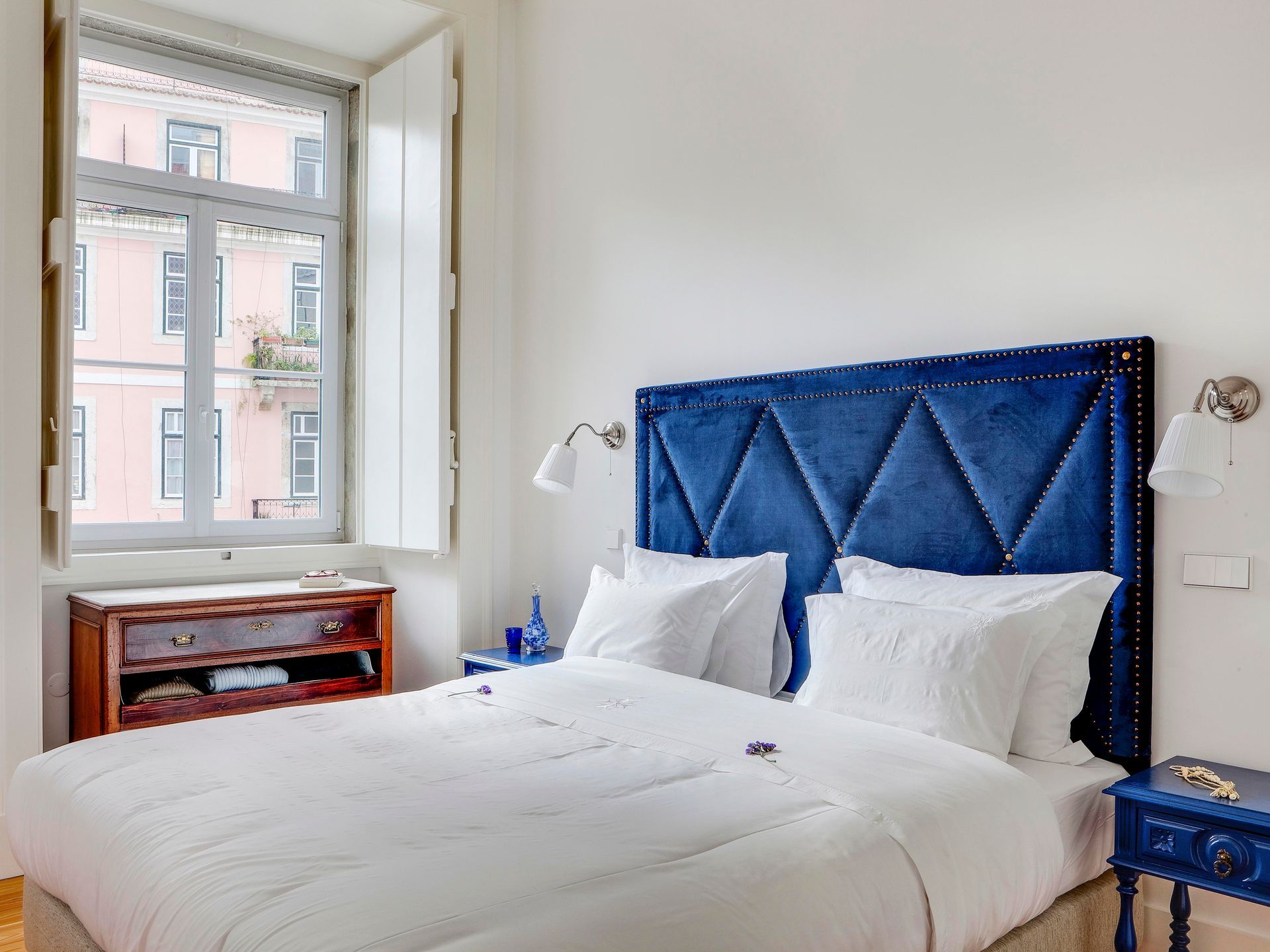 Elegant bedroom in a deluxe one-bedroom apartment with a blue velvet headboard and large windows.