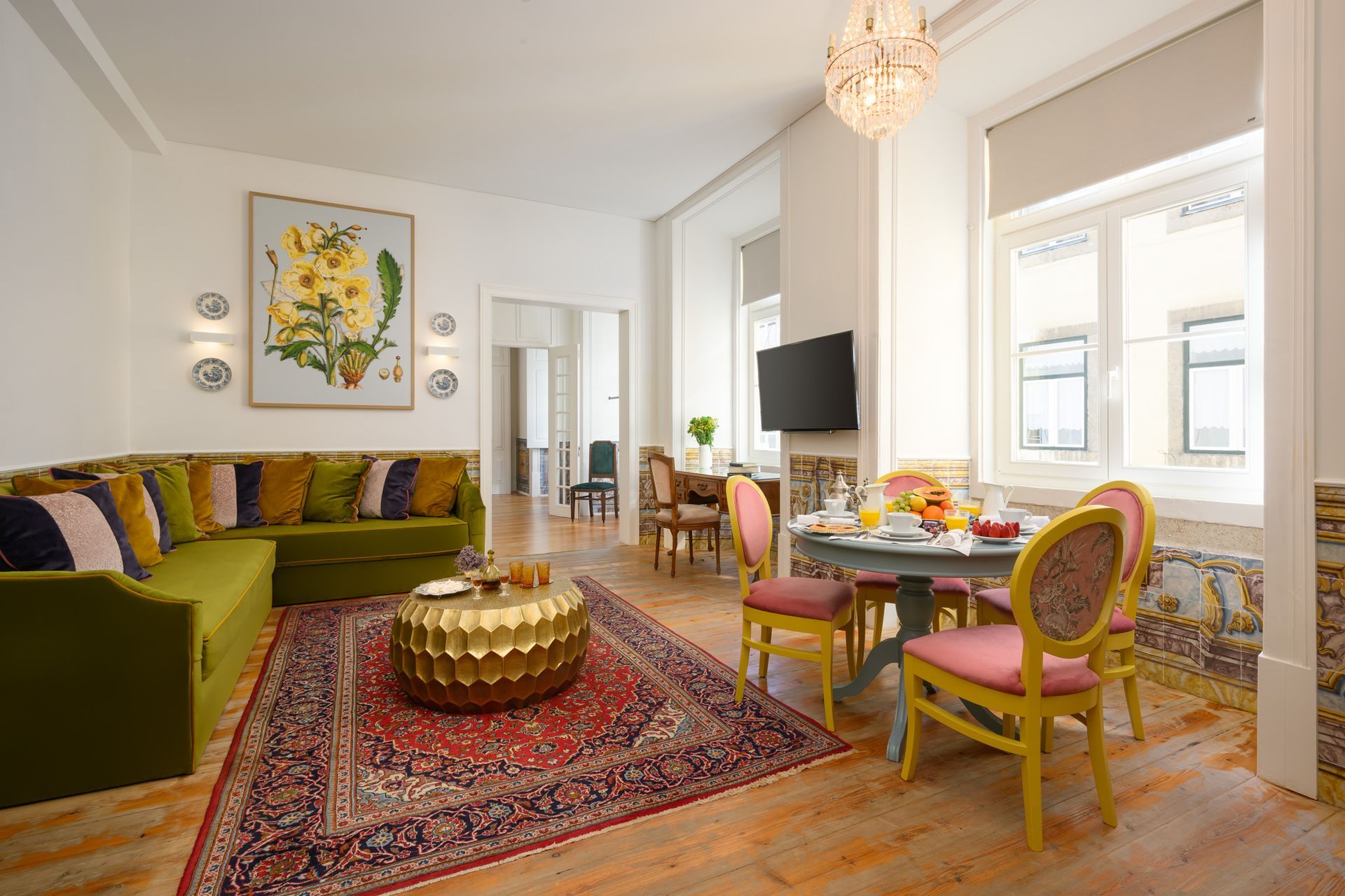 Living room with green sofa, round table, ornate rug, and floral art.