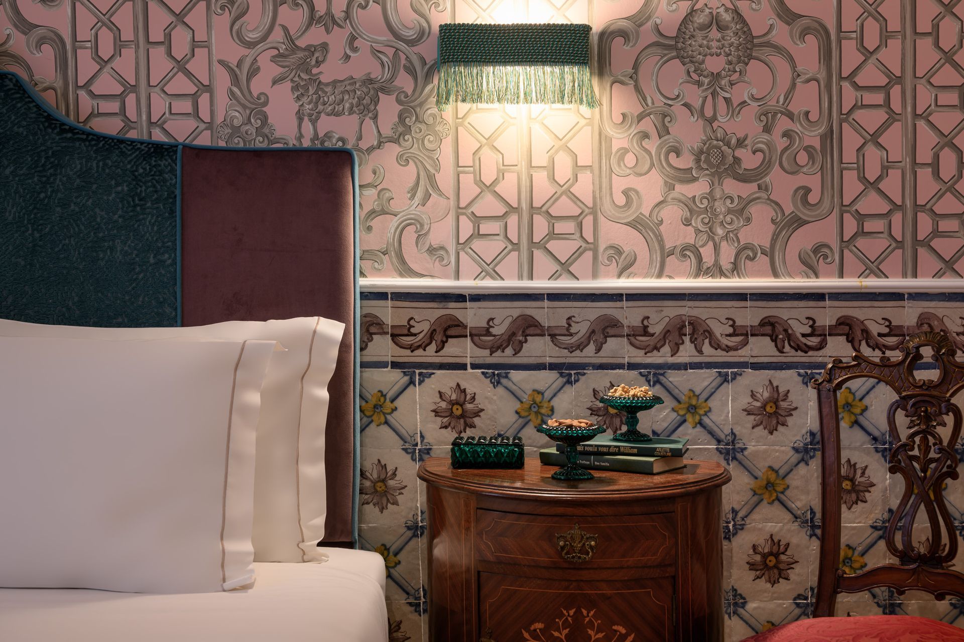 Bedroom interior with patterned wallpaper, tile accents, antique furniture, and a bedside lamp.