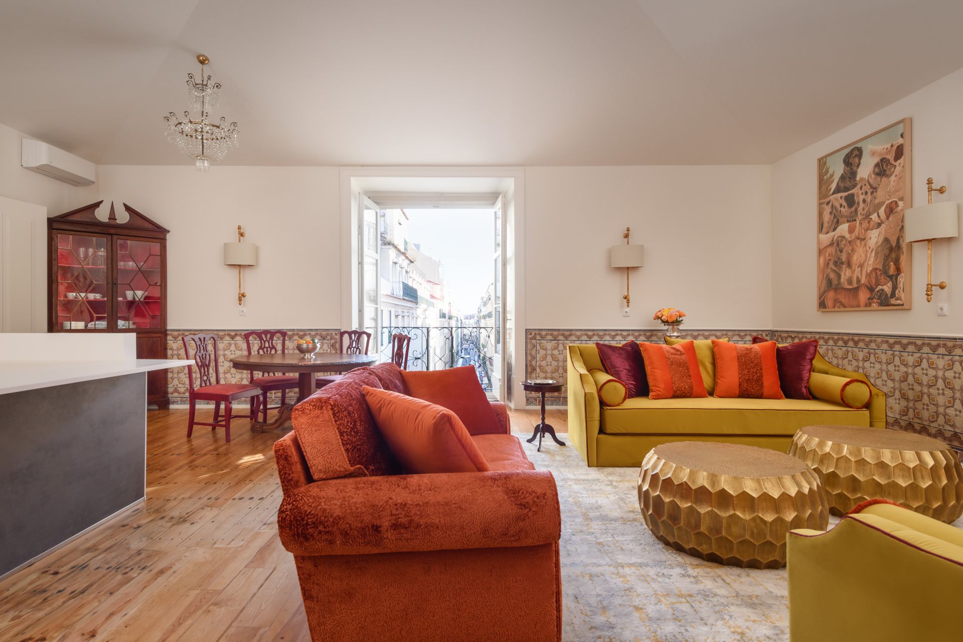 Living room with orange and yellow sofas, dining table, balcony, gold accents, and patterned tile.