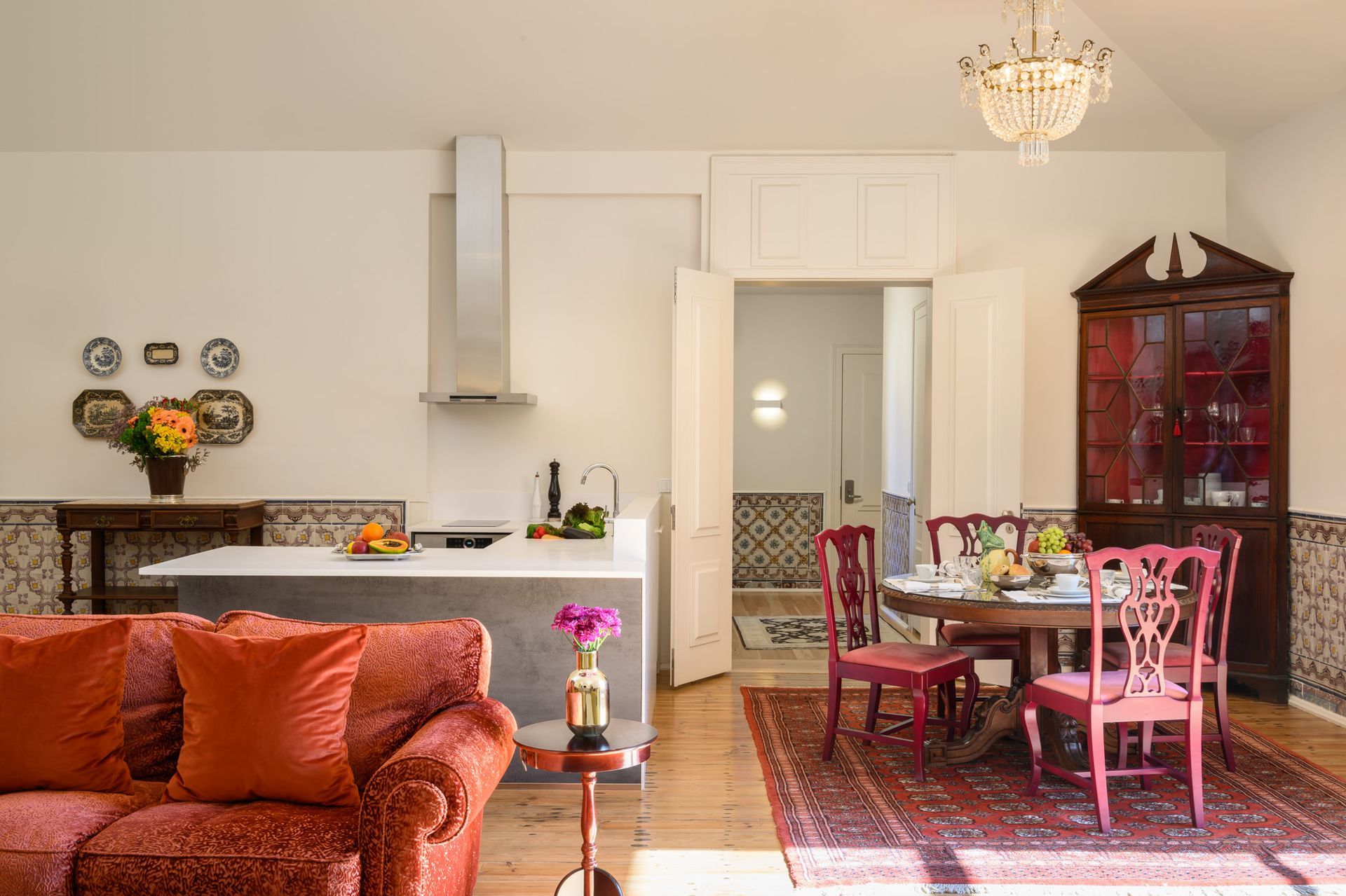 Cozy open-plan living space with kitchen, dining area, red sofa, oriental rug, and antique cabinet.