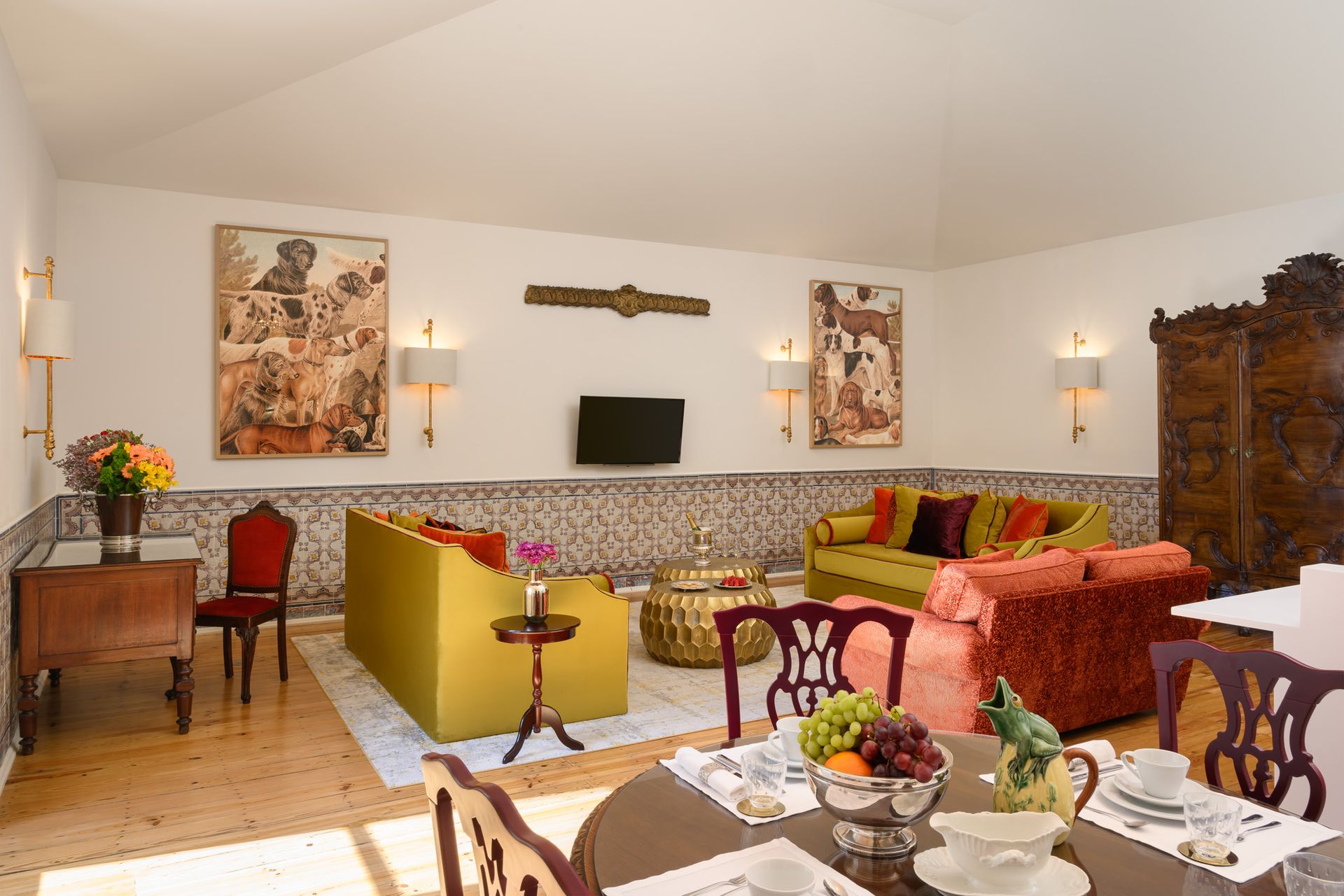 Spacious living room with colorful sofas, antique furniture, artwork, and a dining table set for a meal.