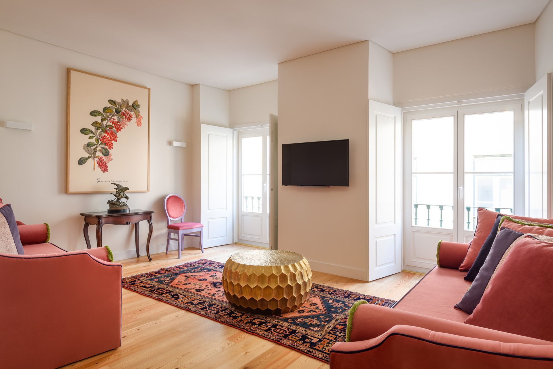 Living room with red sofas, a gold coffee table, artwork, and a TV mounted on a white wall.