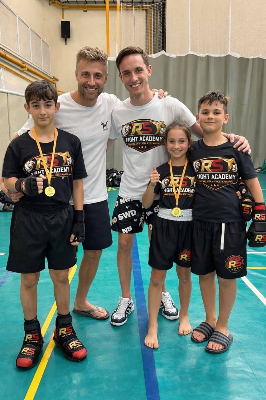 Un grupo de personas en un gimnasio posa tras una competición de artes marciales. Llevan medallas y guantes, sonriendo.