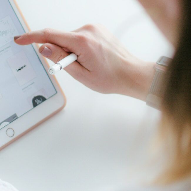 La mano de una mujer utiliza un lápiz óptico en una tableta; el reloj de pulsera es visible.