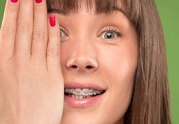 Una mujer con aparatos ortopédicos se cubre el ojo con la mano.