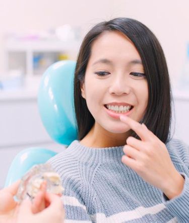 Una mujer está sentada en una silla dental mirando un modelo de sus dientes.