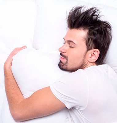 Un hombre está durmiendo en una cama con la cabeza sobre una almohada.