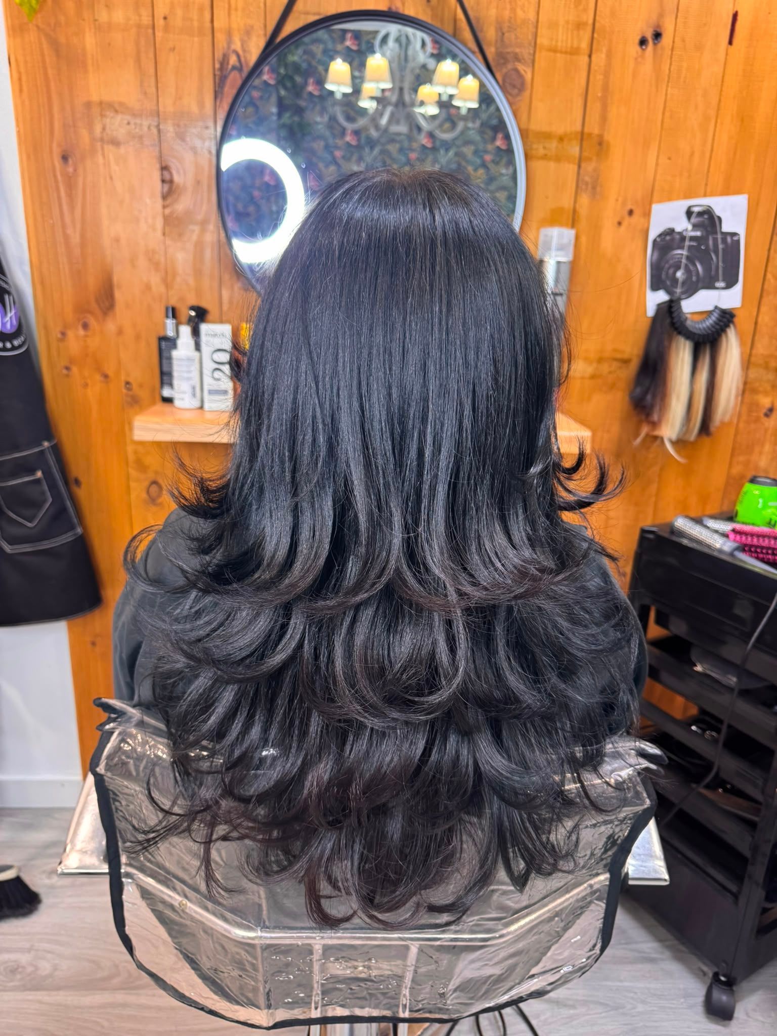 Hombre con cabello oscuro peinado hacia atrás, sentado en una silla de peluquería, visto desde atrás.