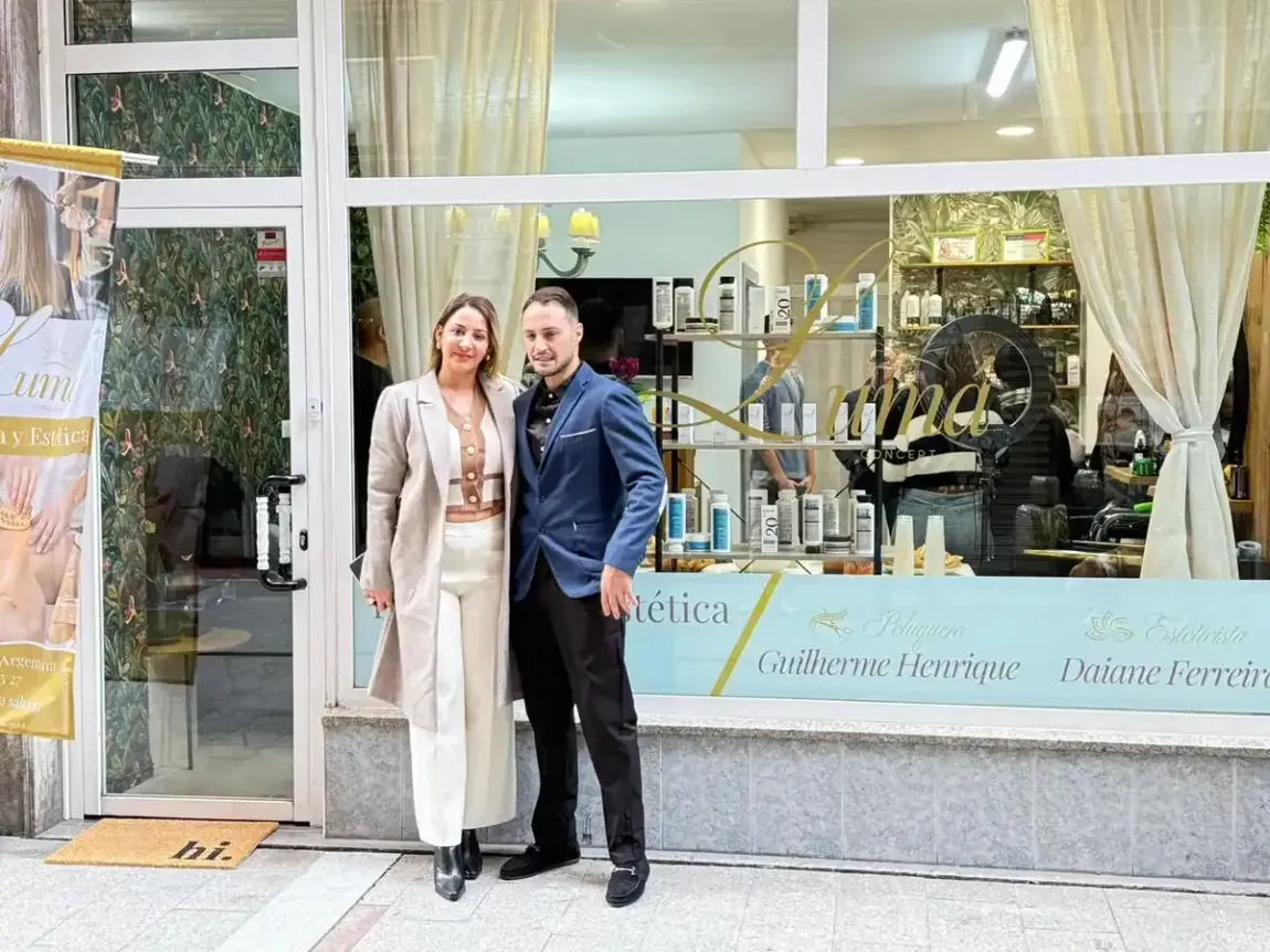 Dos personas de pie, cogidas del brazo, frente a un local comercial con grandes ventanales y cortinas.