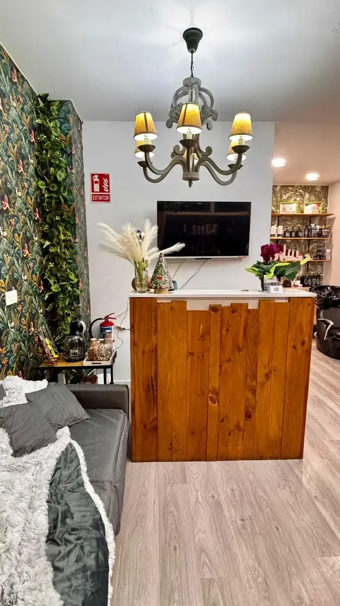 Vestíbulo acogedor con pared floral, lámpara de araña, mostrador de recepción de madera, televisor y zona de estar.