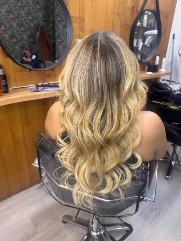 Cabello ondulado castaño dorado con reflejos miel, visto desde atrás en una silla de peluquería.