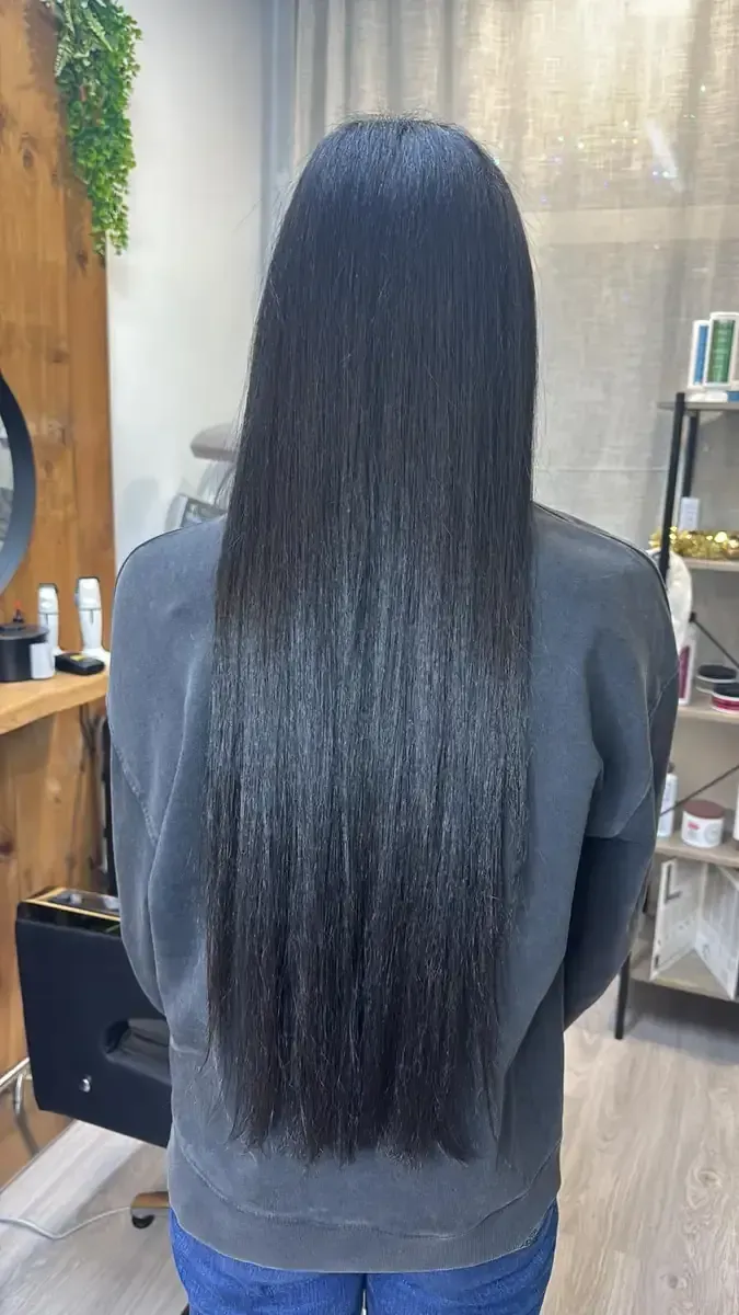Vista trasera de una persona con cabello largo, liso y negro sentada en una silla de peluquería.