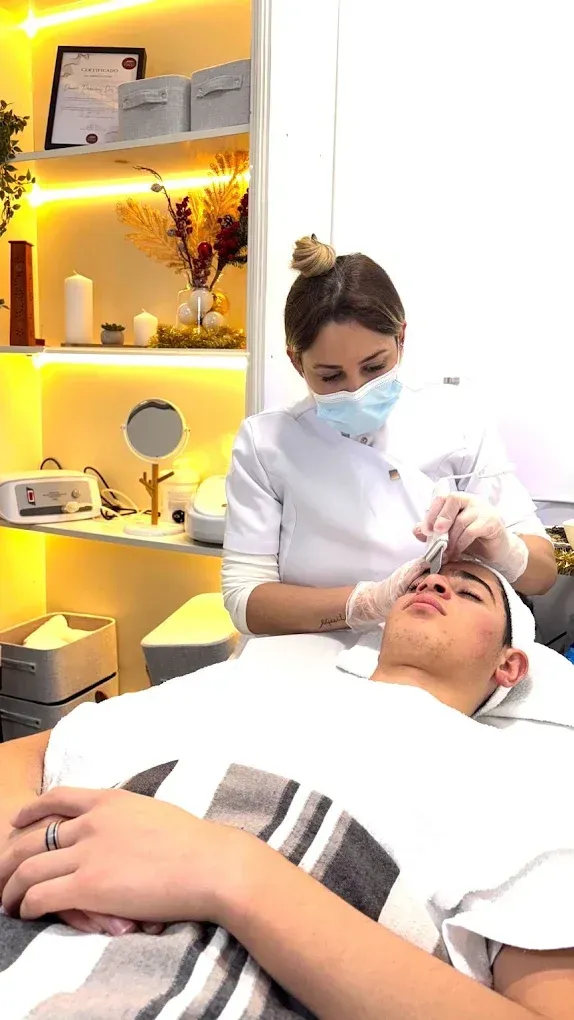 Tratamiento en una clínica de estética con un profesional enmascarado que aplica cuidados faciales a un cliente recostado.