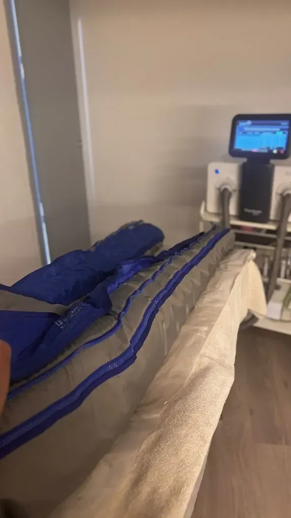 Cama de hospital con manta azul junto a equipo médico y un pequeño monitor en una habitación clínica.