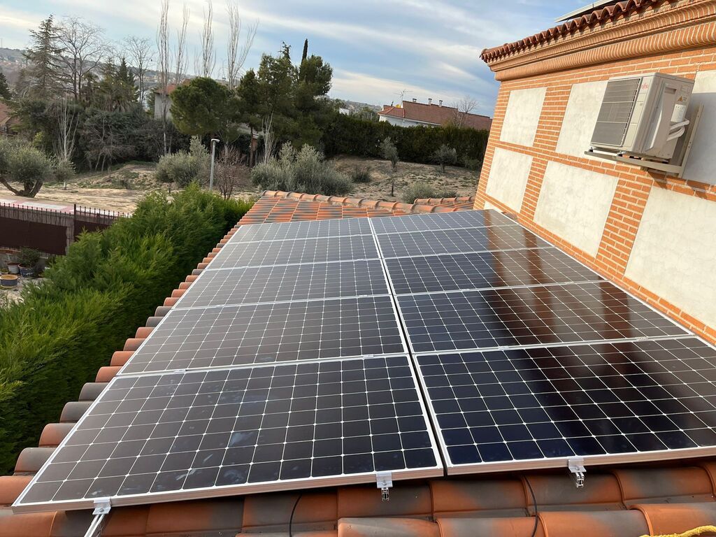 Paneles solares instalados en un tejado de tejas rojas con un aparato de aire acondicionado cerca. Vistas a un paisaje verde.