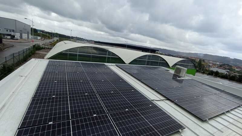 Paneles solares en un tejado, con estructuras de techo blancas curvas y un cielo nublado al fondo.