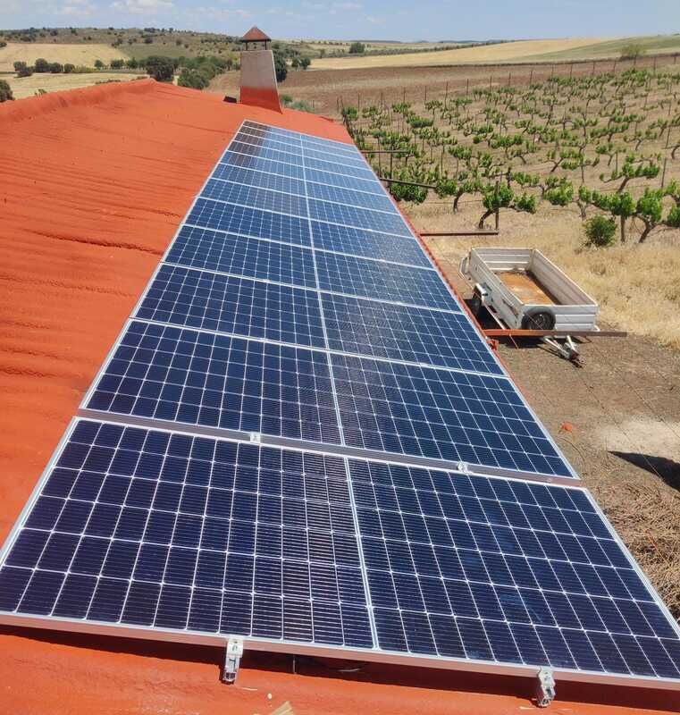 Paneles solares sobre un tejado de tejas rojas, viñedo al fondo, día soleado.