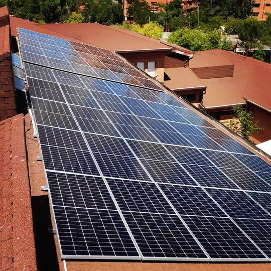 Paneles solares instalados en un tejado marrón rojizo, que proporcionan energía renovable. Día soleado, barrio residencial.