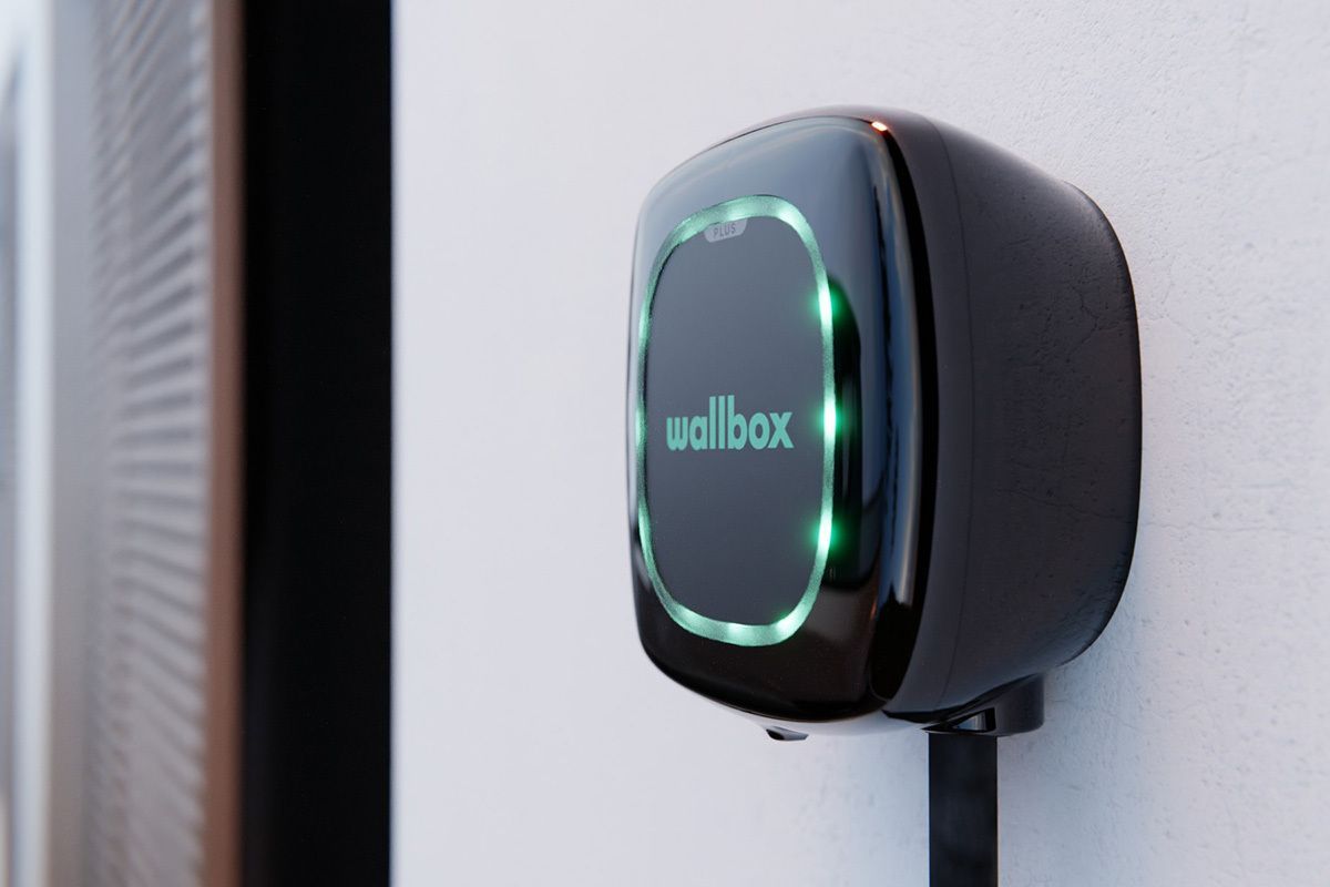 Cargador EV Wallbox negro montado en una pared blanca, iluminado con luces verdes.