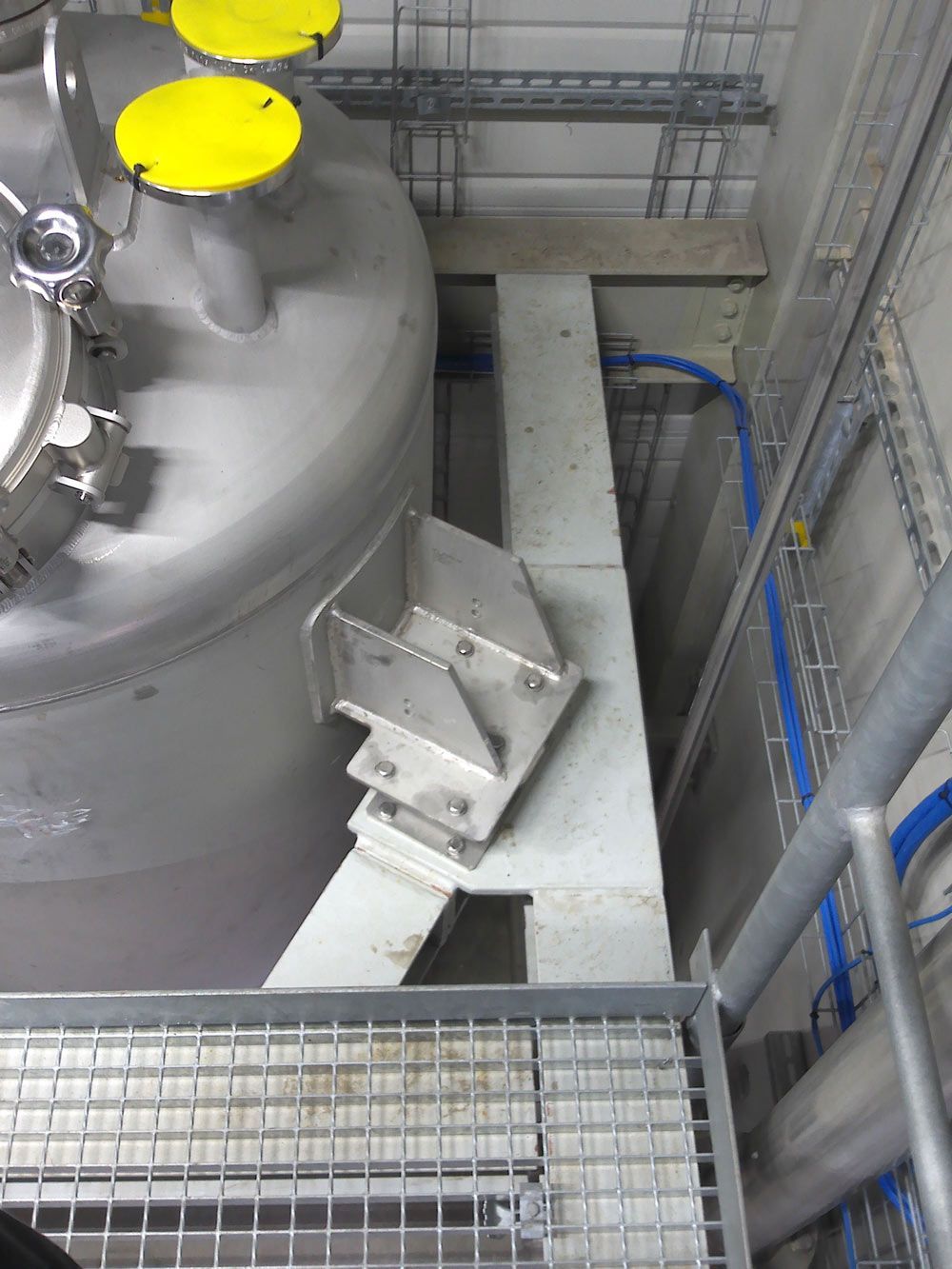 Auf einer Metallplattform steht ein Edelstahltank mit gelben Deckeln.