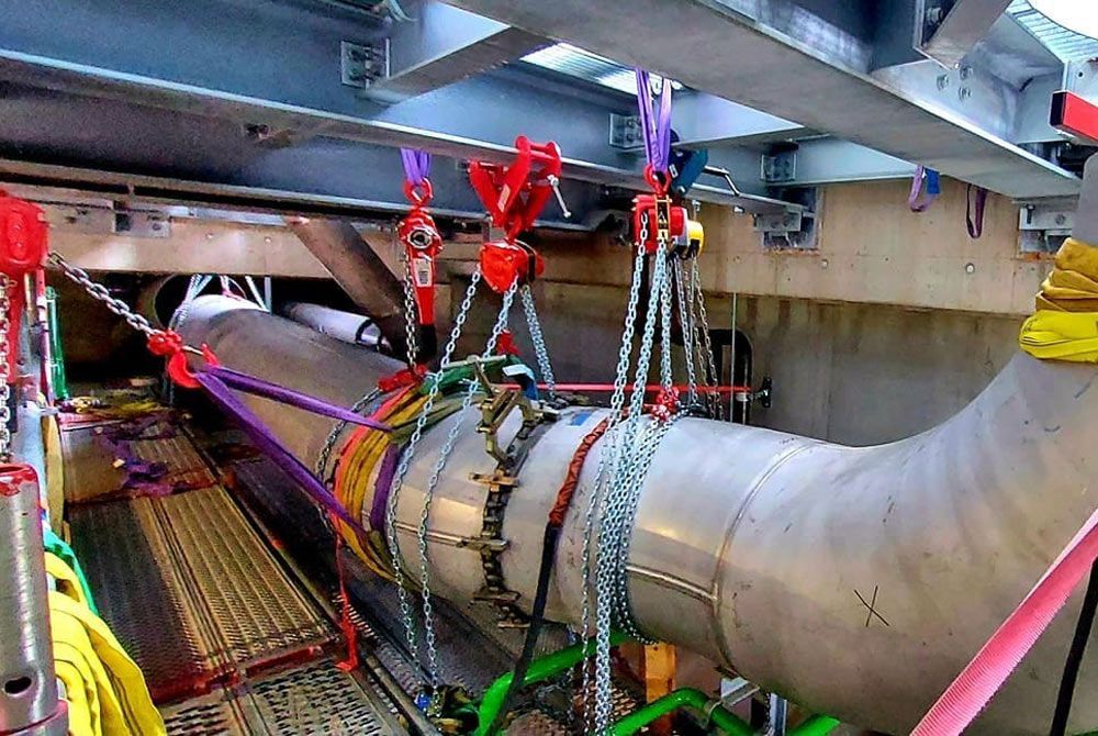 Ein großes Rohr wird mithilfe von Ketten und Seilen angehoben.