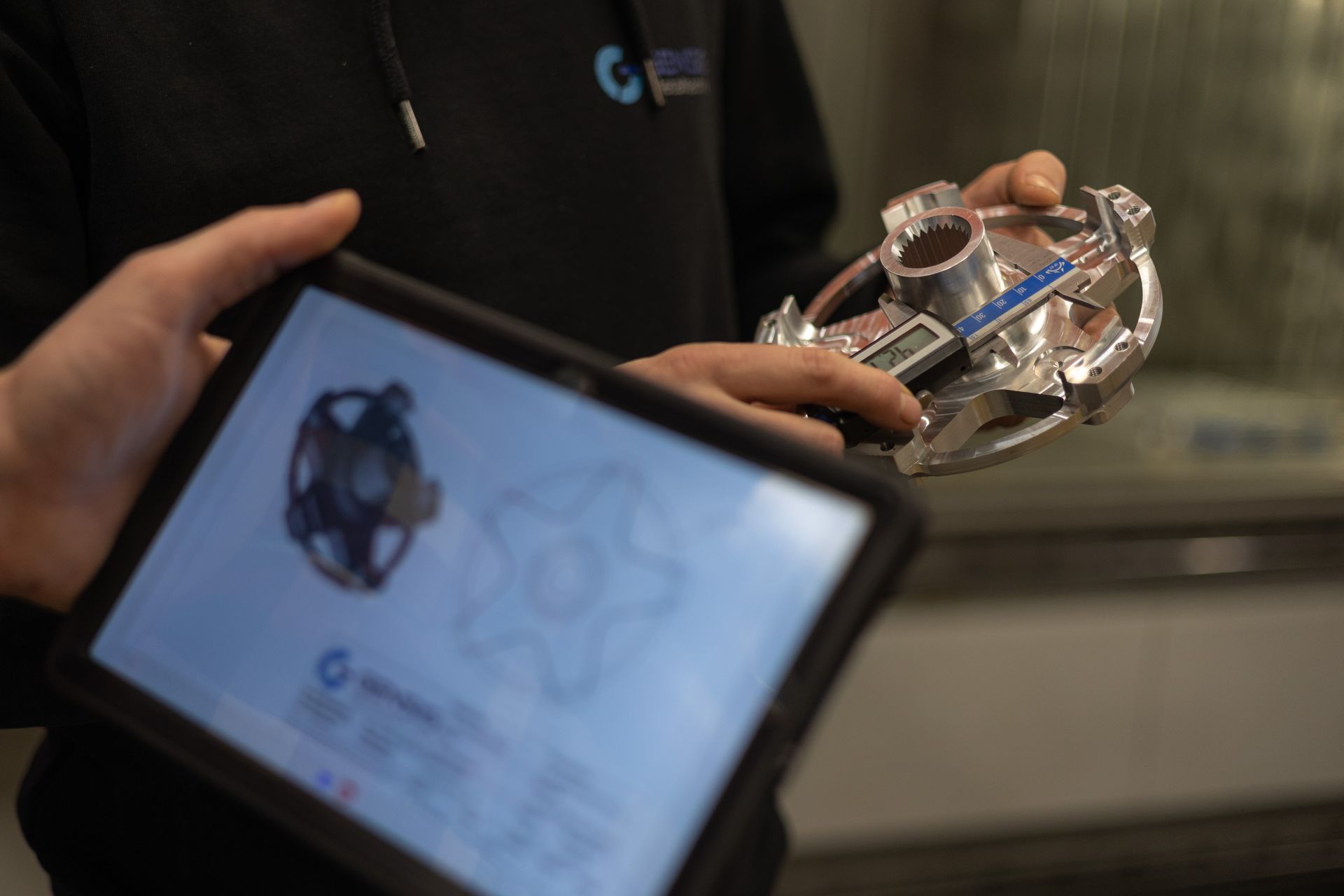 ein Mitarbeiter hält ein Tablet in der Hand und zeigt auf ein Metallteil .