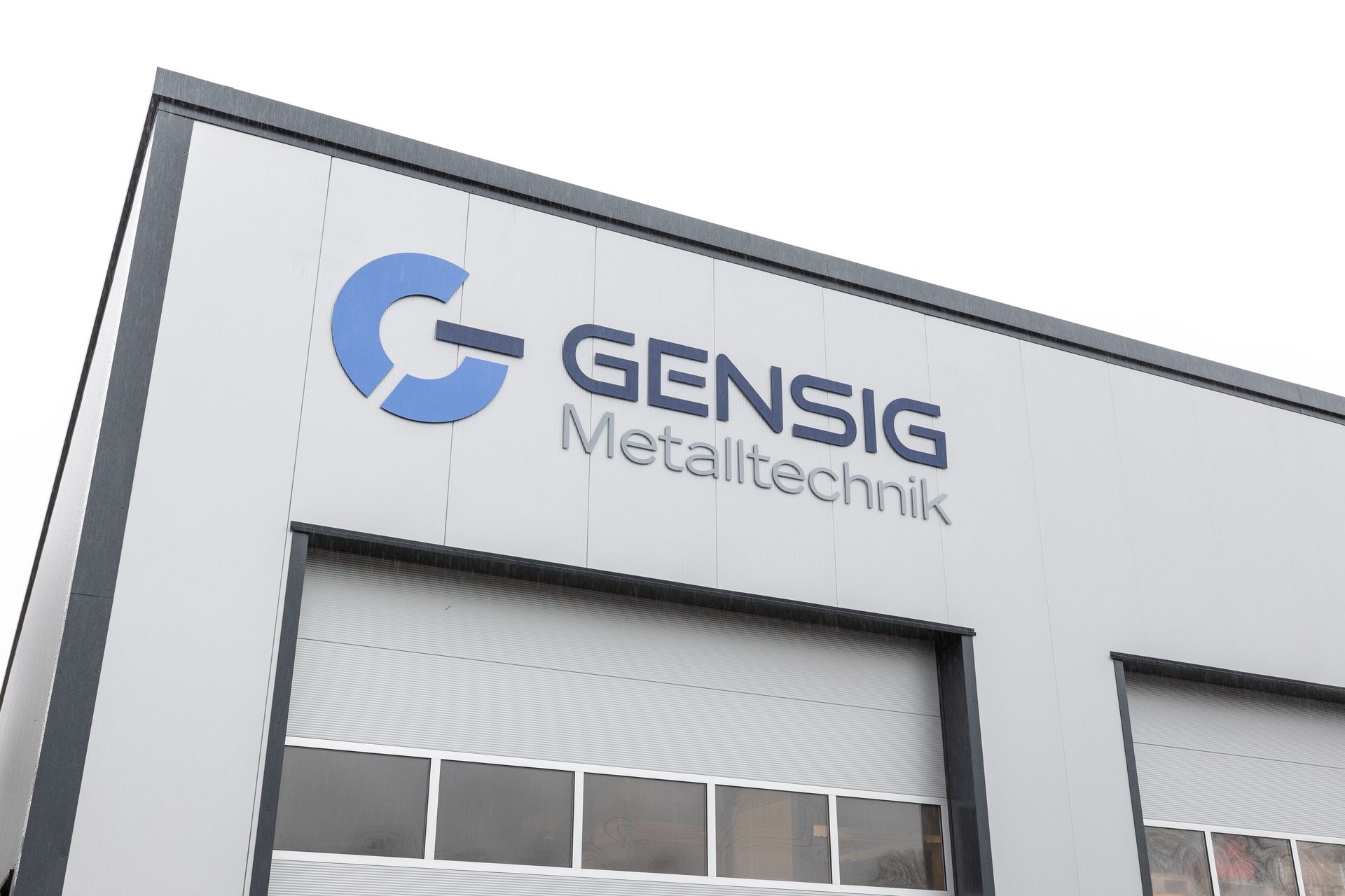 eine moderne Lagerhalle von außen, mit dem Logo Gensig Metalltechnik darauf.
