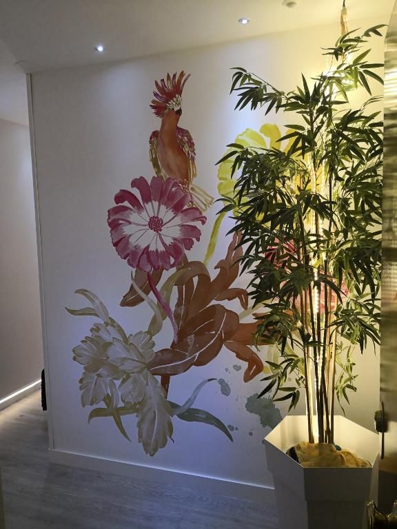 Mural de una flor y un gallo junto a una planta de bamb煤 en maceta en un pasillo moderno.