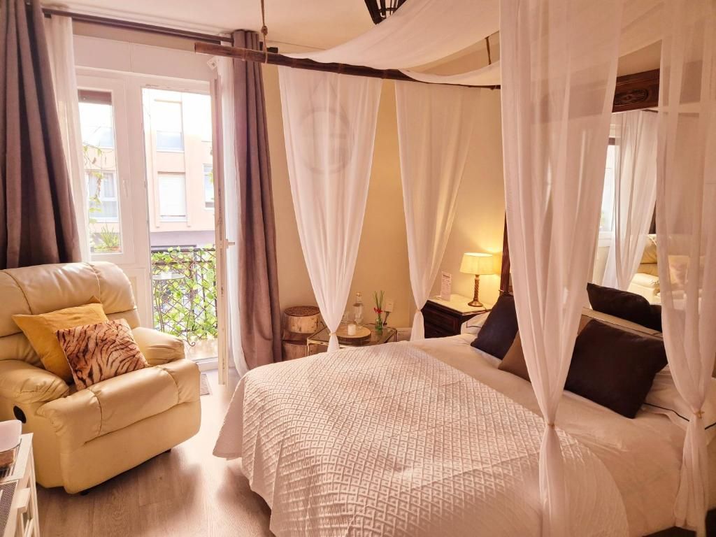 Acogedora habitación con cortinas de dosel transparentes, ropa de cama blanca, sillón 