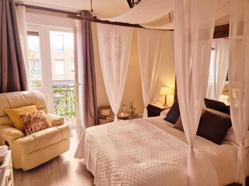 Acogedora habitaci贸n con cortinas de dosel transparentes, ropa de cama blanca, sill贸n