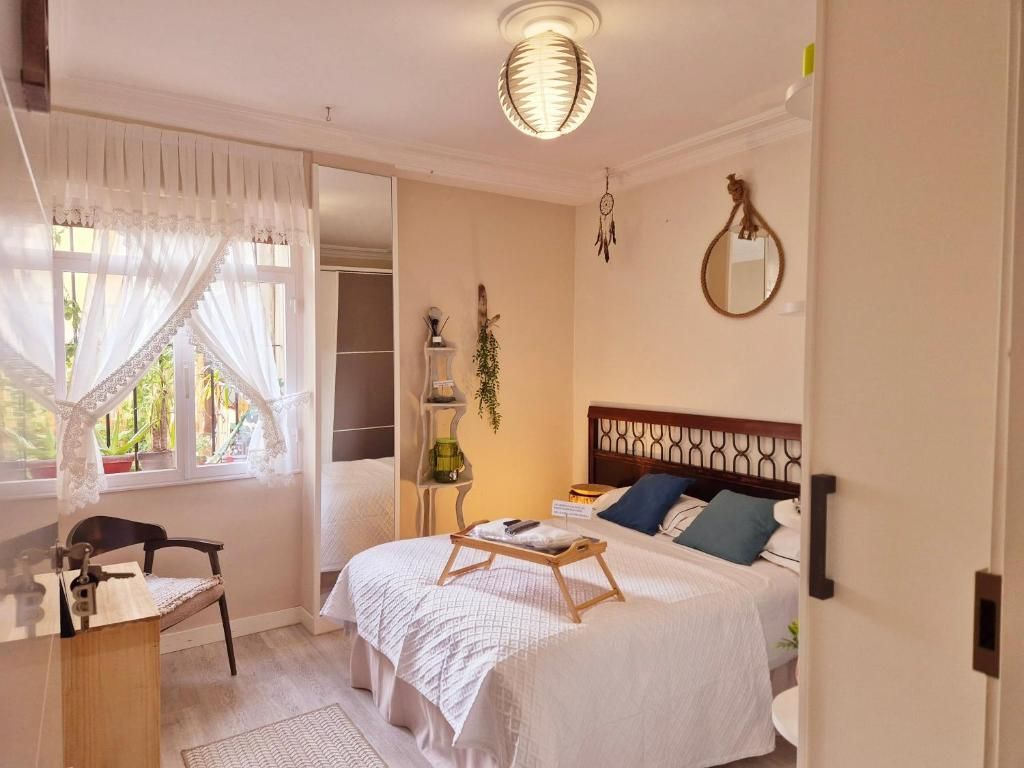 Habitación luminosa con ropa de cama blanca, silla de madera, espejo colgante y luz natural 