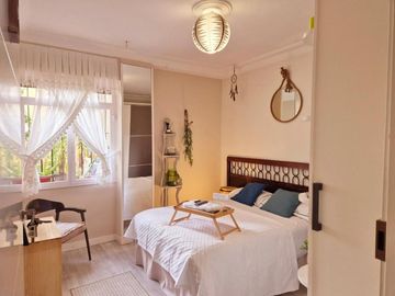 Habitaci贸n luminosa con ropa de cama blanca, silla de madera, espejo colgante y luz natural
