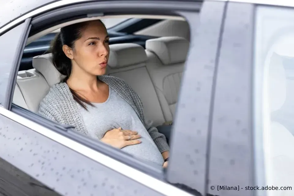 Eine schwangere Person sitzt auf dem Rücksitz eines Autos, schaut aus dem Fenster und hält sich den Bauch.